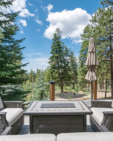 Patio with wicker seating, fire table, and umbrella overlooking pine forest and mountains