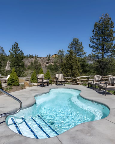 Hot tub surrounded by concrete patio with striped lounge chairs, umbrella, and pine forest with mountain views