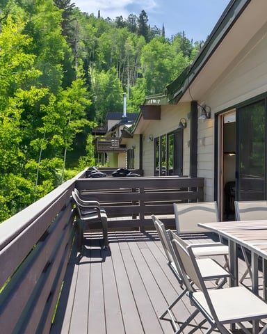 Modern deck with dining table and chairs overlooking dense green forest and distant houses