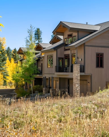 Modern mountain home with brown siding and stone accents surrounded by golden aspen trees and dry grass in autumn