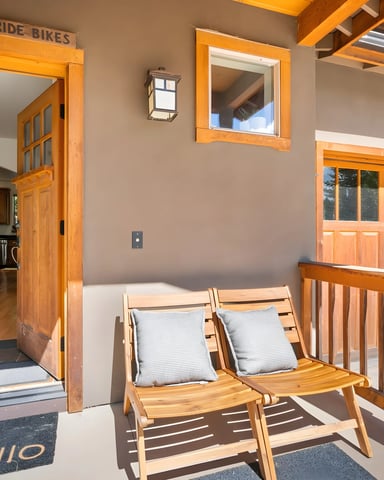 Covered porch with wooden lounge chairs, open door to kitchen, and wooden garage door with windows