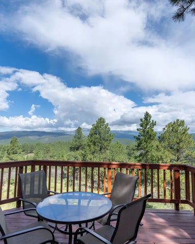 Wooden deck with table and chairs overlooking forested mountains and valley under blue sky