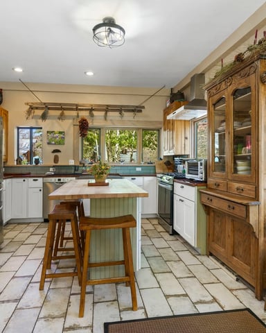 Spacious kitchen with white cabinetry, stainless steel appliances, center island with seating, and large windows overlooking desert landscape.