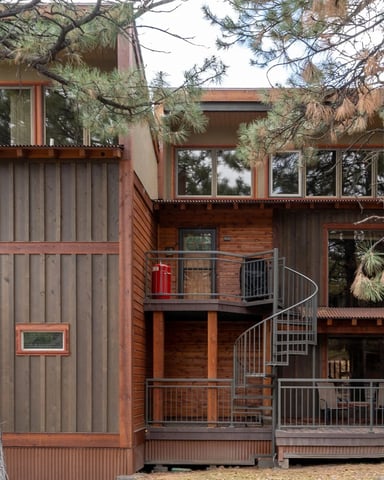 Modern multi-level cabin with red metal siding and large windows nestled among tall pine trees