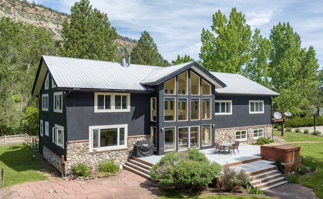 Large dark-sided home with hot tub, patio, and mountain backdrop